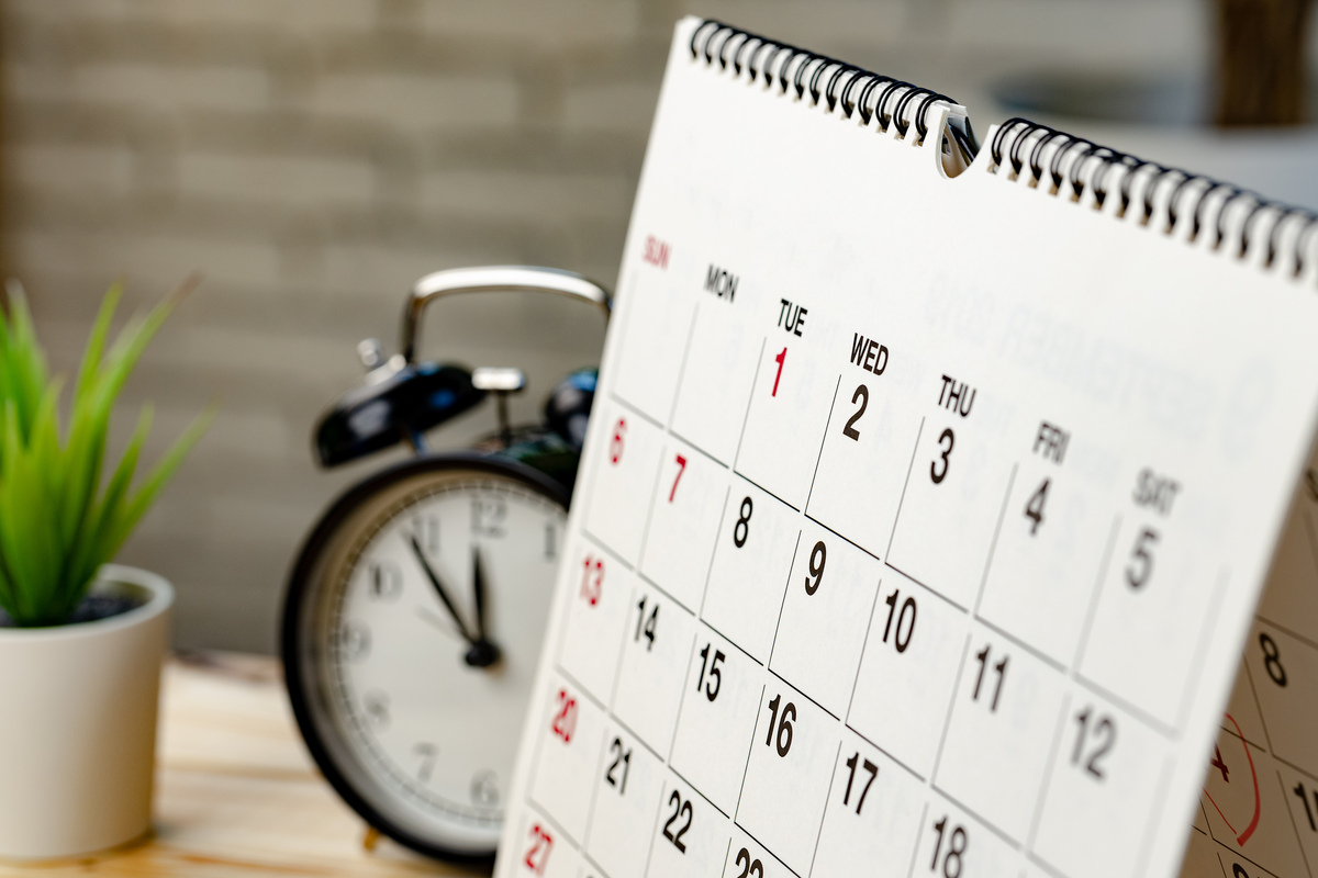 close up of calendar page on a desk with an alarm clock in the background