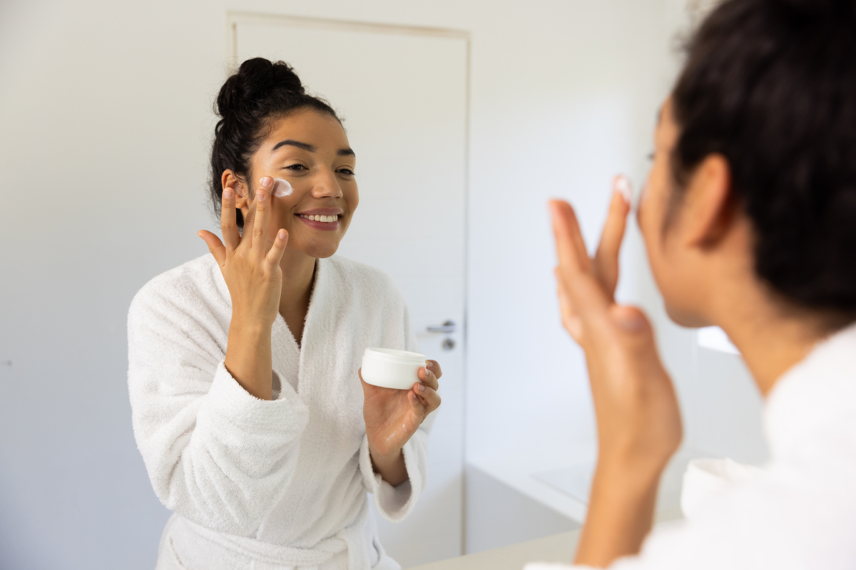 woman looking in mirror applying face cream