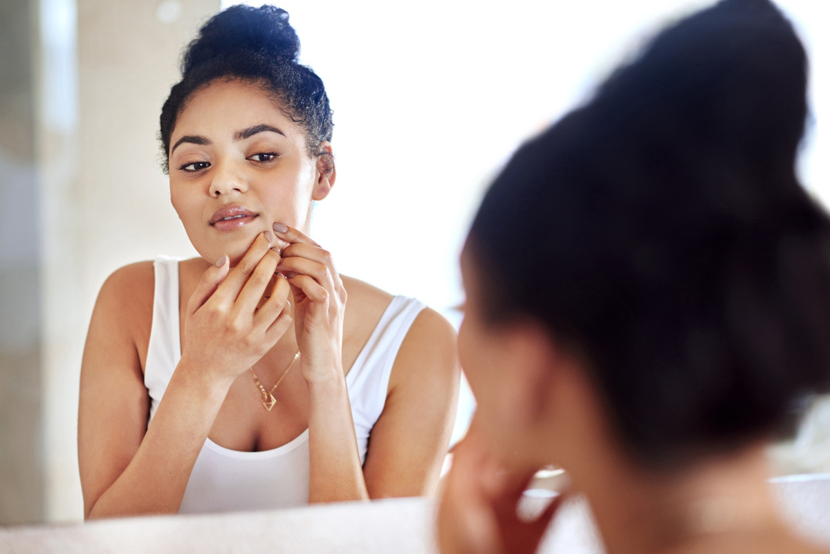 woman looking in mirror examining a blemish on her chin