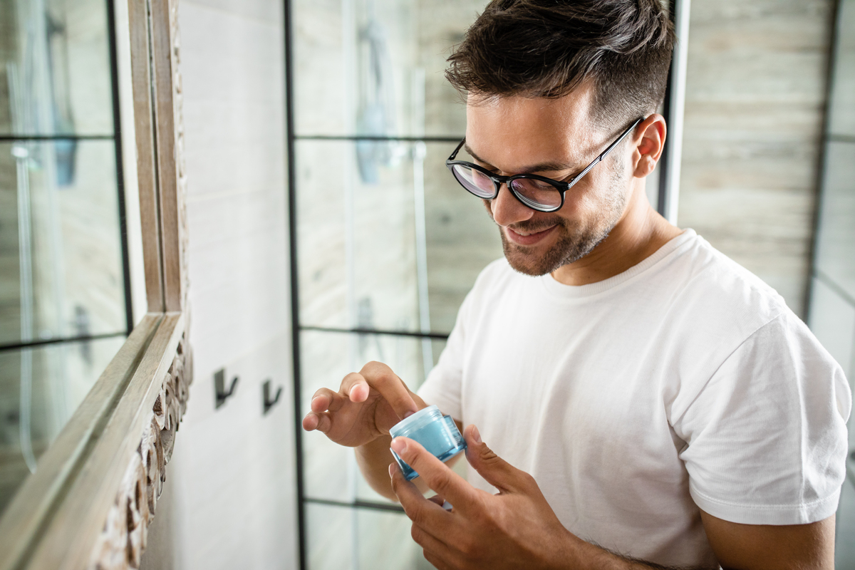 man standing in front of mirror about to apply skincare