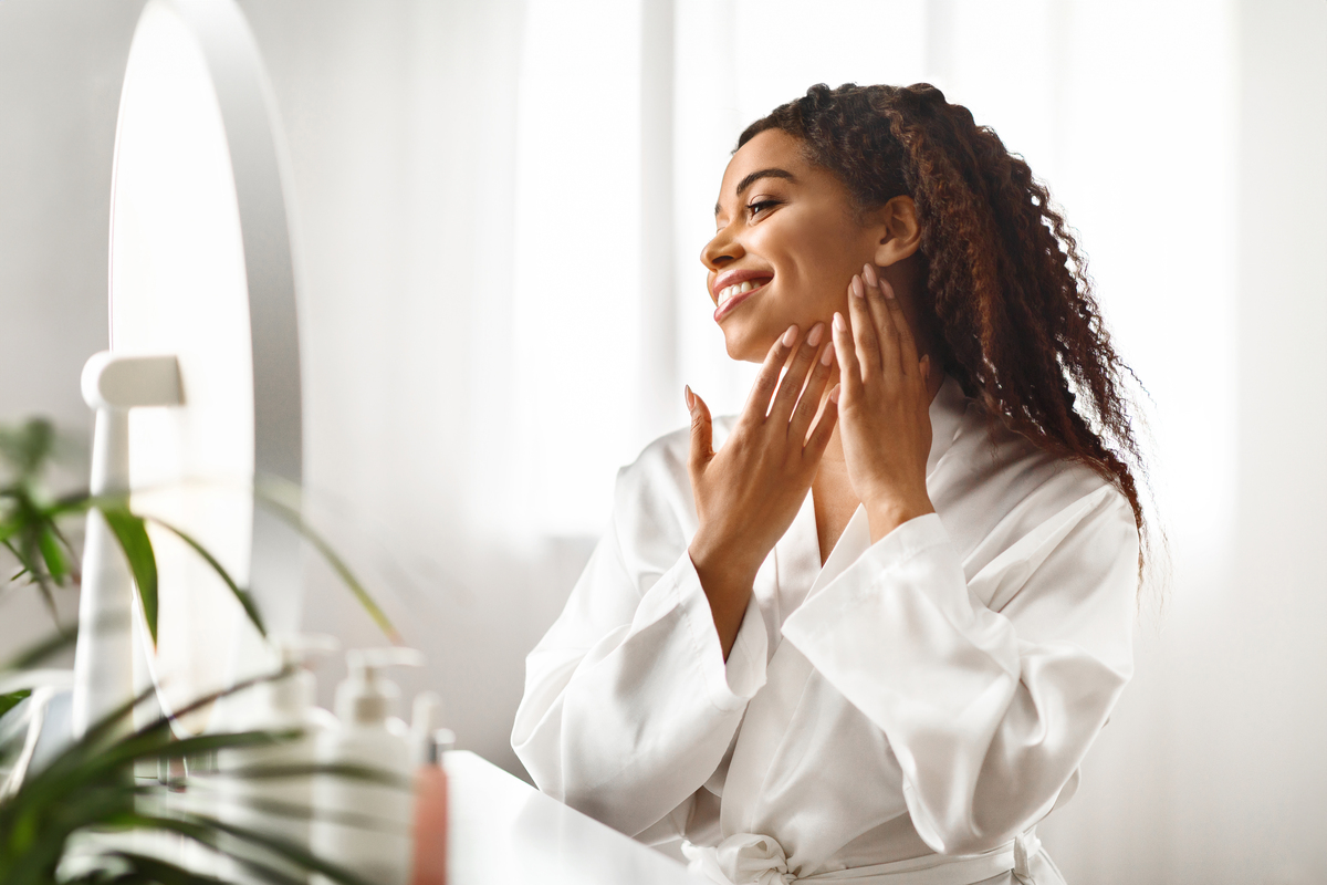 woman in bathrobe applying skincare products to face while smiling