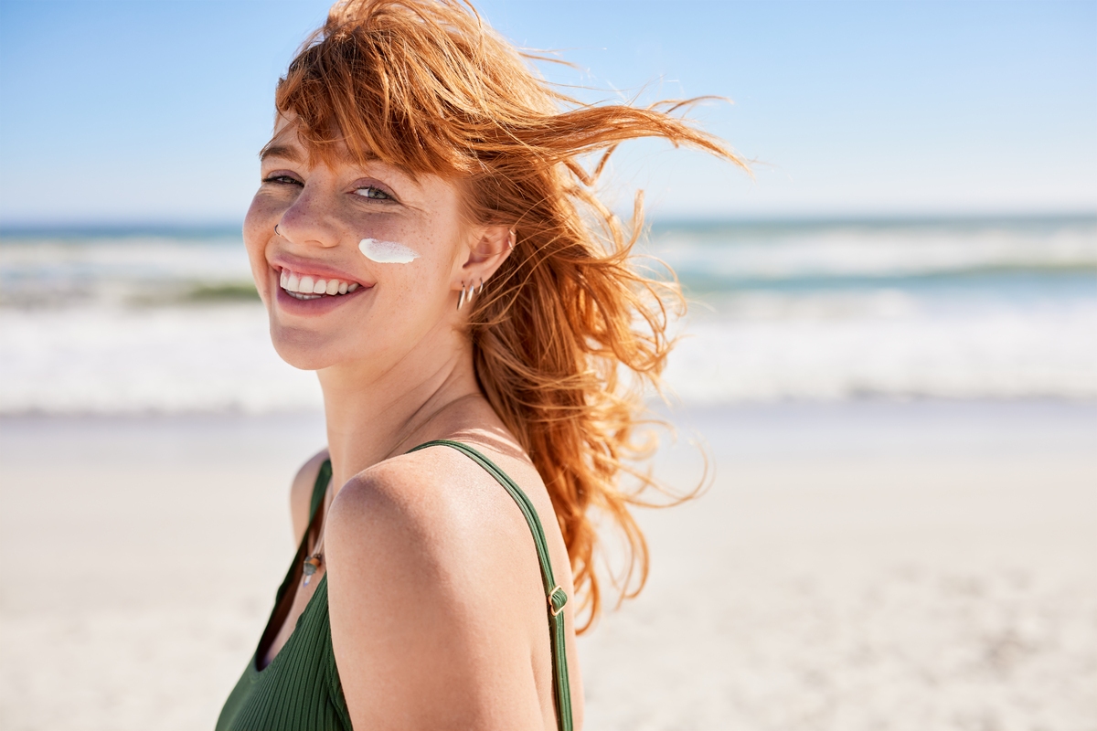smiling woman with sunscreen on her cheek, standing on a beach