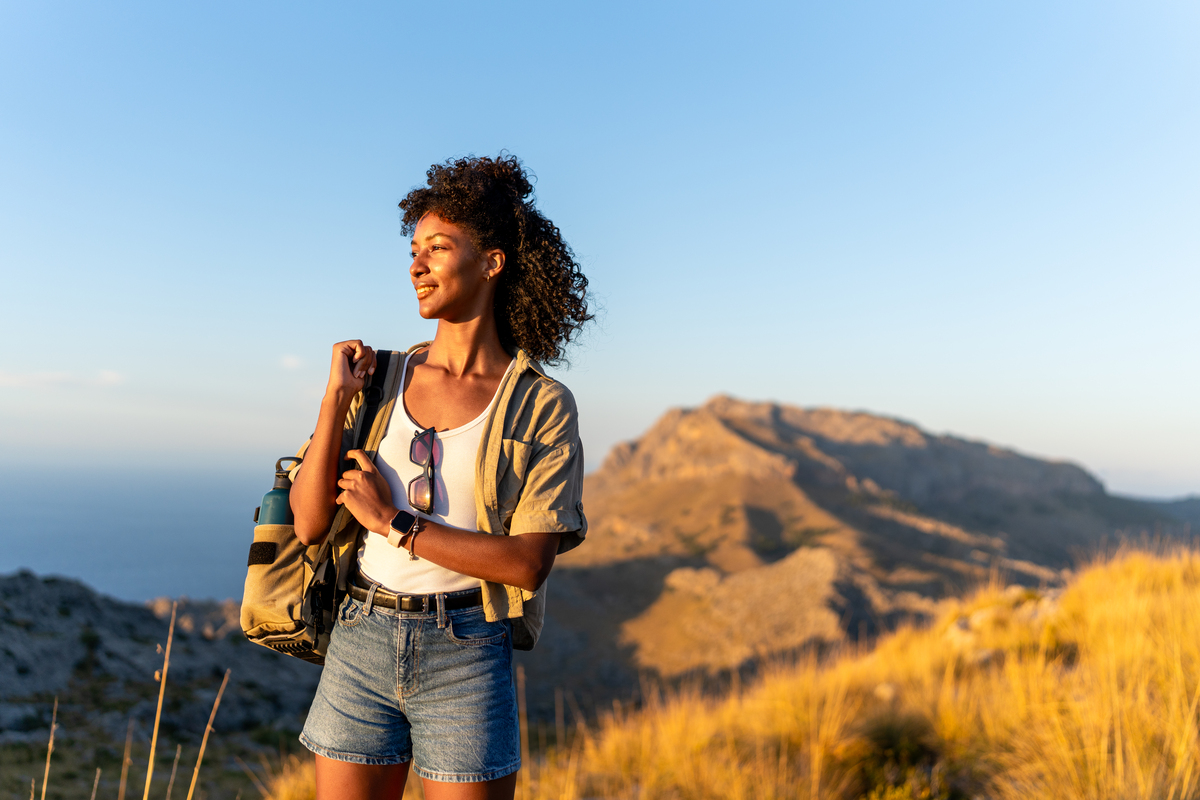 woman hiking in mountains, looking into the distance at sunset