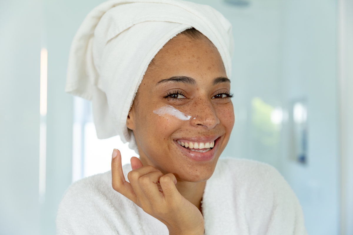 woman smiling applying spf to her cheek in the bathroom